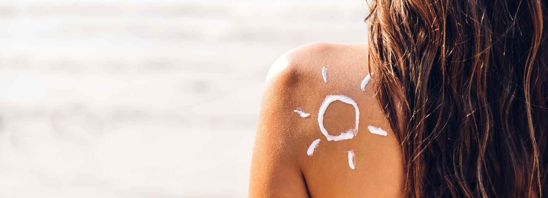 Frau im zweiteiligen Bikini trägt Sonnencreme auf und wird von der Sonne gezeichnet