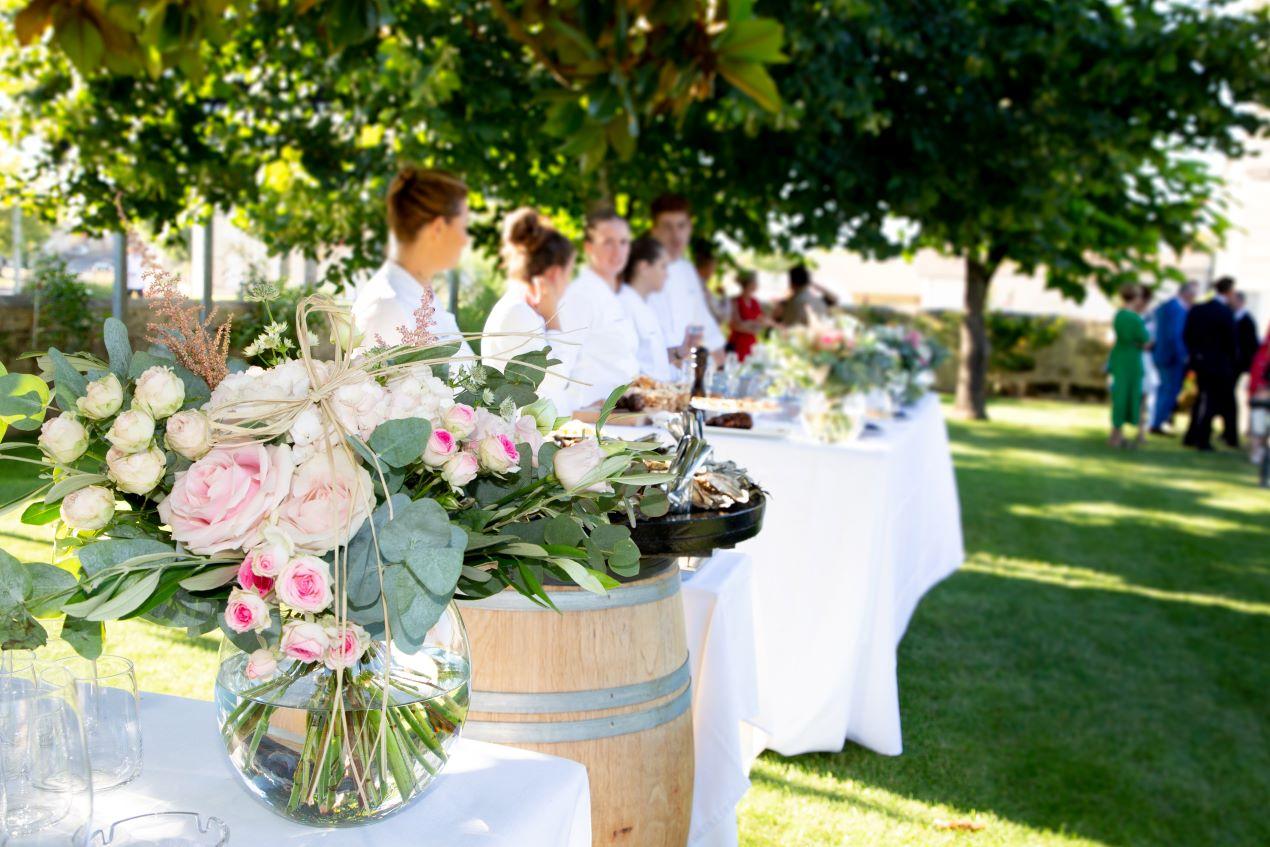 Blumenarrangement auf einem Holzbottich vor einem Buffet im Freien, geeignet für eine Bauernhof Feier oder eine Gartenparty