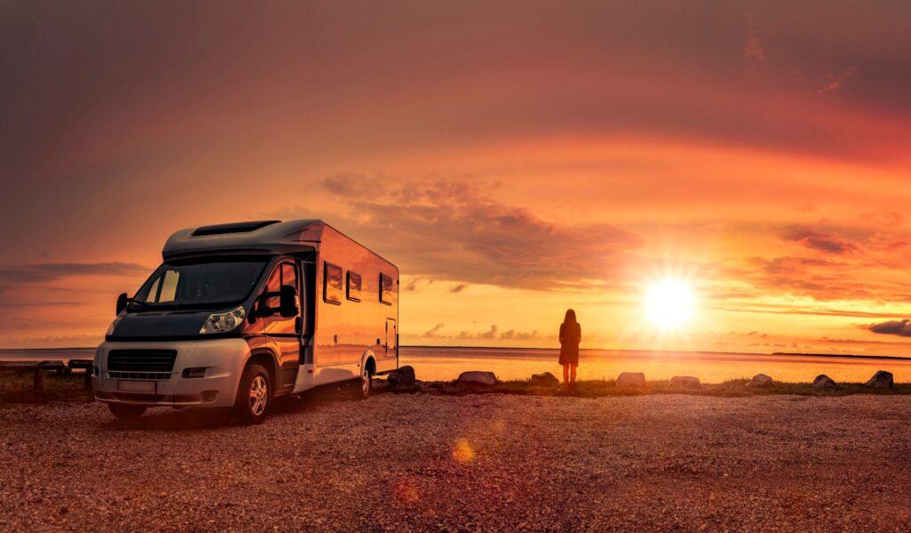 Ein modernes Wohnmobil bei Sonnenuntergang, geparkt an einem malerischen See. Eine Person steht in der Ferne und genießt die Aussicht, symbolisch für nachhaltiges Reisen ohne Plastik.