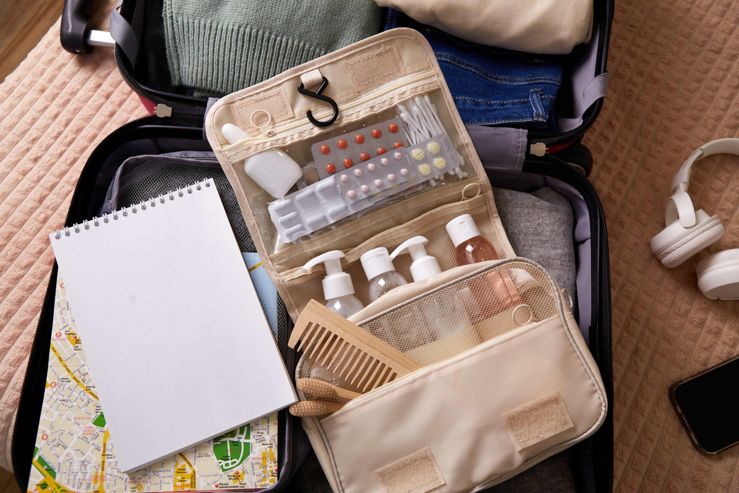 Offene Reisetasche, gefüllt mit Kleidung, Toilettenartikeln und Reiseutensilien, bereit für eine Reise. Nahaufnahme.