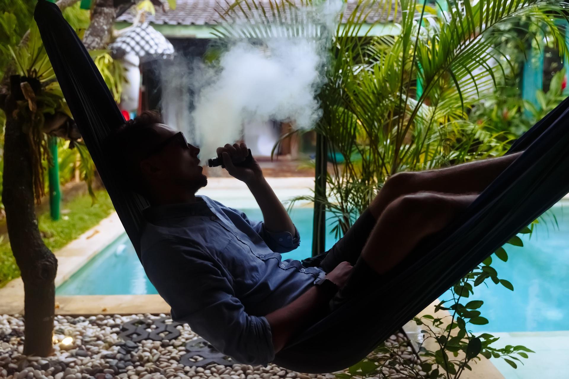 Mann dampft in Hängematte am Pool | Elf Bar Vape