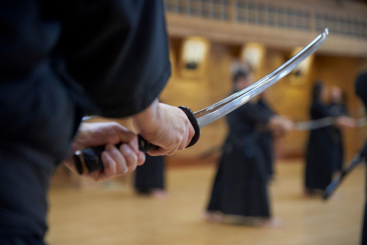 Menschen beim Schwertkampftraining in Japan, die traditionelle Katana halten, mit Fokus auf die Schwertgriffe in einer Dojo-Umgebung.